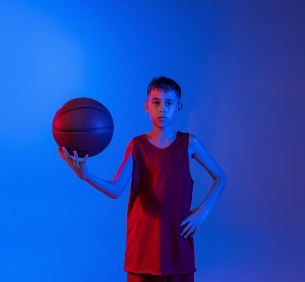 Retrato de um menino jogador de basquete posando isolado sobre um fundo gradiente azul roxo em néon