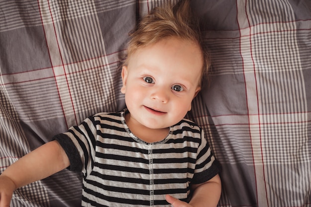 Retrato de um menino loiro bonito de seis meses, deitado em uma cama cinza