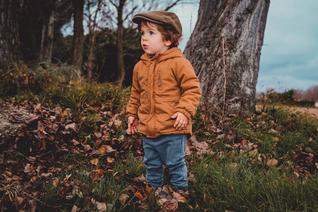 Retrato de um menino loiro caucasiano com um casaco laranja de outono no campo em um dia nublado.