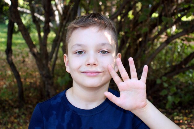 Foto retrato de um menino loiro de 9 anos em um parque de outono com uma camiseta azul mostra sua palma