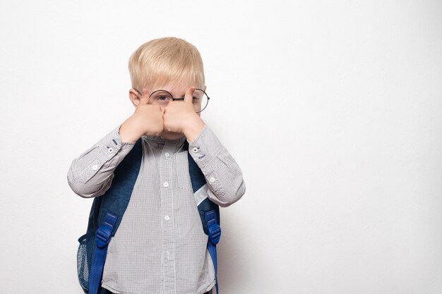 Retrato de um menino loiro de óculos e com uma mochila escolar mostra uma aula de gesto. Conceito de escola