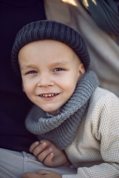 Retrato de um menino no outono com um chapéu de malha sentado com os pais em um campo