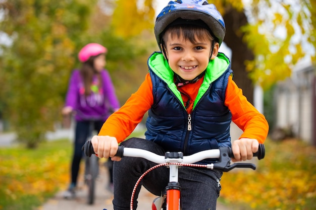 Foto retrato de um menino no parque com sua irmã na parede. criança pequena usando um capacete e andando de bicicleta em um dia de outono. esportes ativos e saudáveis ao ar livre.