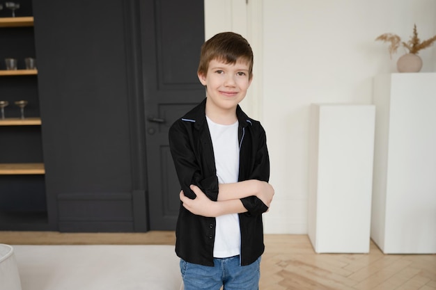 Retrato de um menino pré-escolar feliz em uma camisa preta no interior de um apartamento perto de um sofá branco