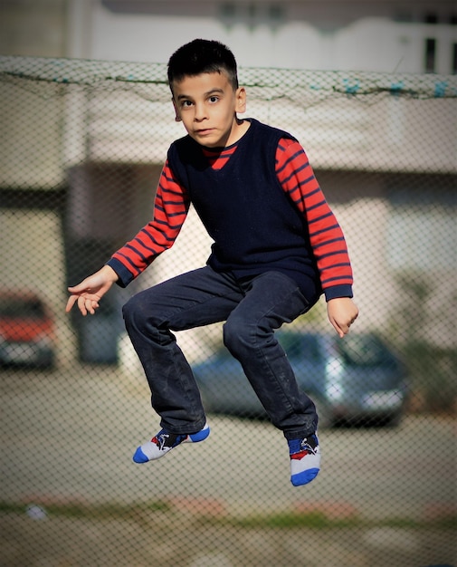 Foto retrato de um menino pulando contra uma cerca de cadeia