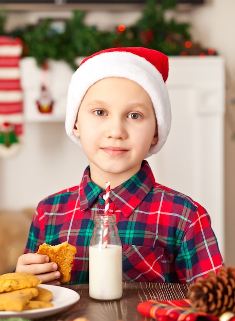 Retrato de um menino segurando um biscoito de Natal e bebendo leite.