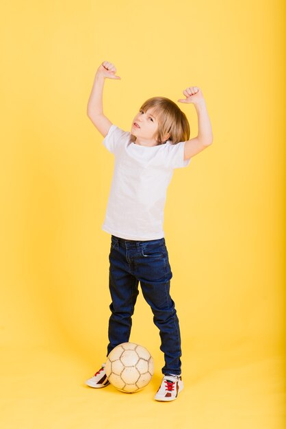 Retrato de um menino segurando uma bola de futebol, fundo amarelo estúdio