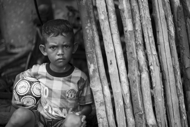 Retrato de um menino sentado com uma bola de futebol por bambu