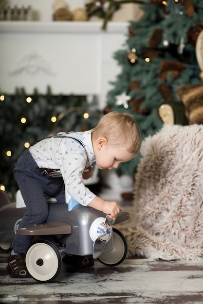 Retrato de um menino sentado em um avião de brinquedo vintage perto de uma árvore de Natal