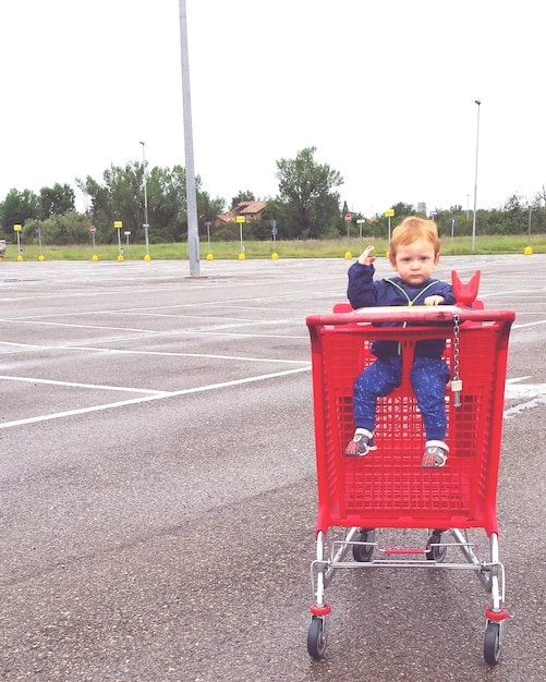 Retrato de um menino sentado em um carrinho de compras contra o céu