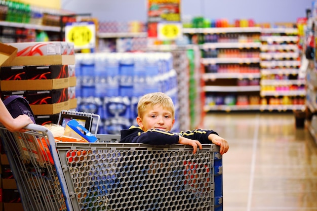 Retrato de um menino sentado em um carrinho de compras em uma loja