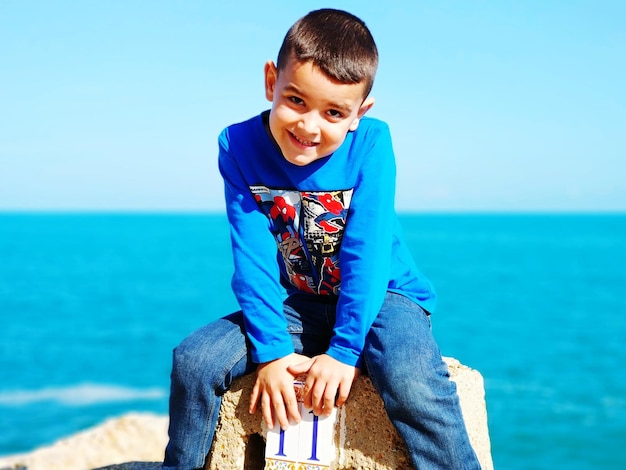 Retrato de um menino sentado na praia contra o céu azul