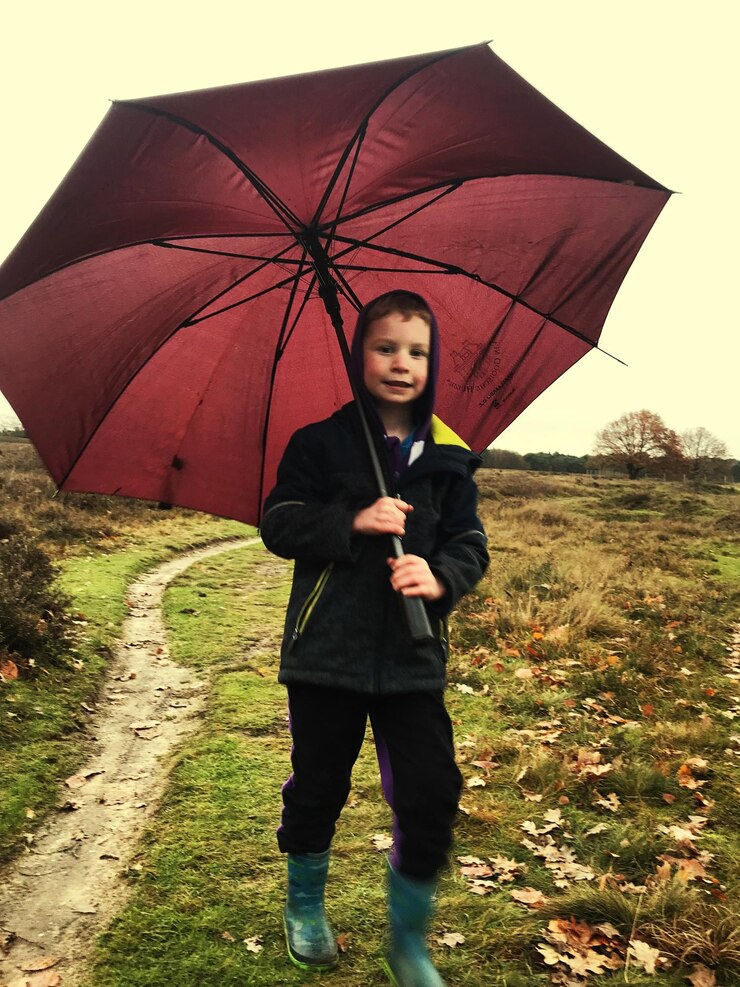 Foto retrato de um menino sorridente caminhando com um guarda-chuva no campo