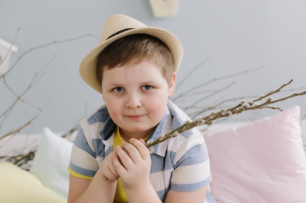 Retrato de um menino sorridente com um chapéu segurando galhos de salgueiro