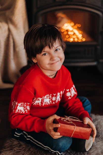 Retrato de um menino sorridente com um presente nas mãos perto da lareira em casa