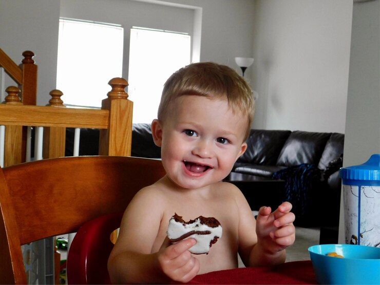 Foto retrato de um menino sorridente comendo sentado em uma cadeira em casa