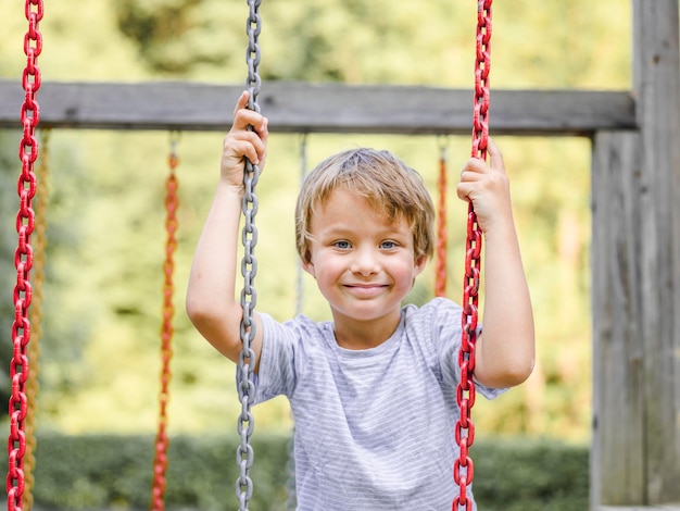 Retrato de um menino sorridente em um balanço no playground