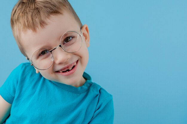 Retrato de um menino sorridente em um óculos engraçados. escola. pré escola. moda. retrato de estúdio em uma parede azul, copie o espaço