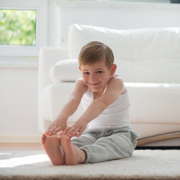 Retrato de um menino sorridente se exercitando sentado no chão em casa