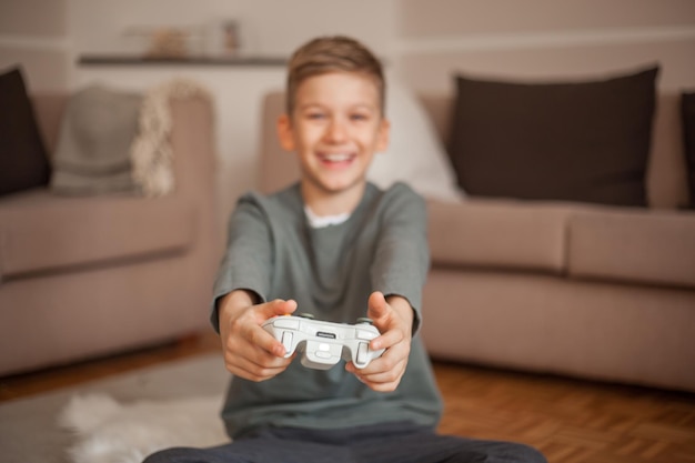 Retrato de um menino sorridente segurando o controle remoto de um videogame na sala de estar de casa