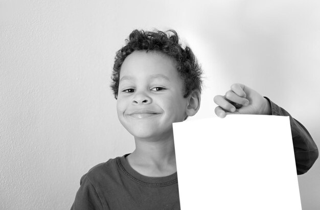 Foto retrato de um menino sorridente segurando papel contra a parede