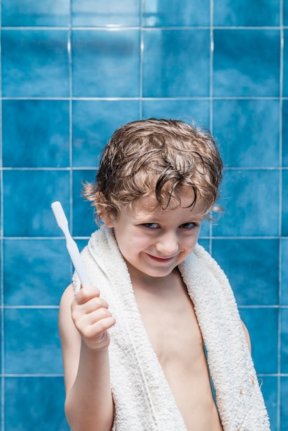Foto retrato de um menino sorridente segurando uma escova de dentes no banheiro