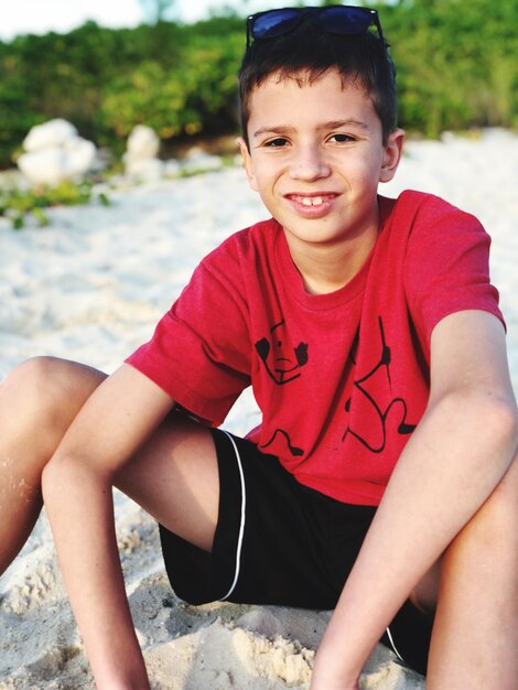 Foto retrato de um menino sorridente sentado na areia ao ar livre