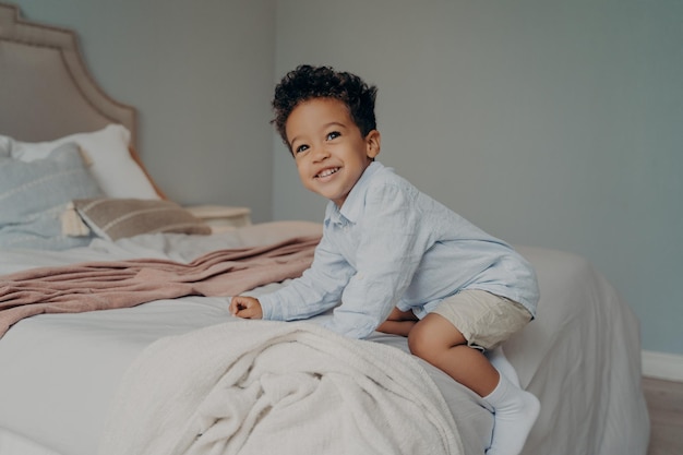 Foto retrato de um menino sorridente sentado na cama em casa