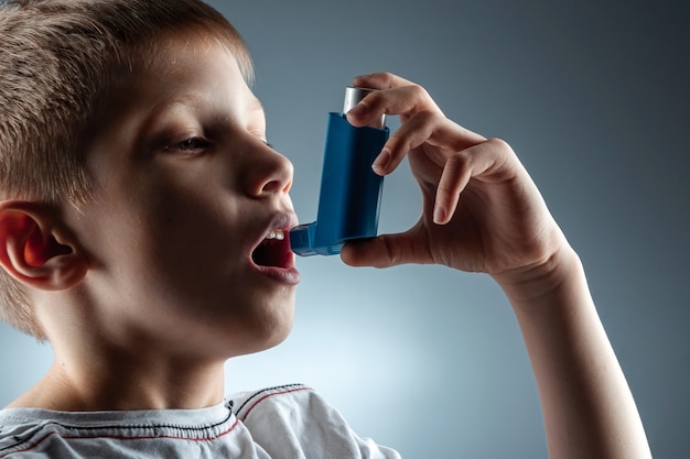 Retrato de um menino usando um inalador de asma para tratar doenças inflamatórias, falta de ar. O conceito de tratamento para tosse, alergias, doenças do trato respiratório.