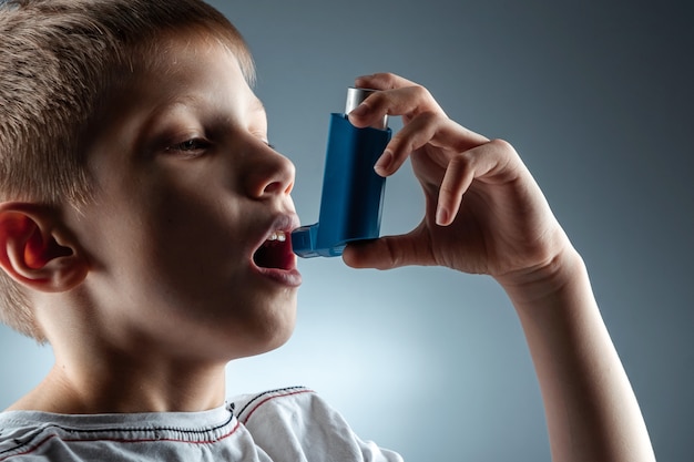 Retrato de um menino usando um inalador de asma para tratar doenças inflamatórias, falta de ar. o conceito de tratamento para tosse, alergias, doenças do trato respiratório.