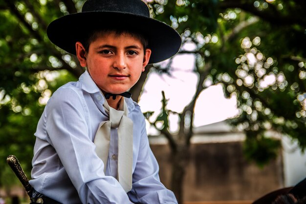 Retrato de um menino vestindo um chapéu contra árvores