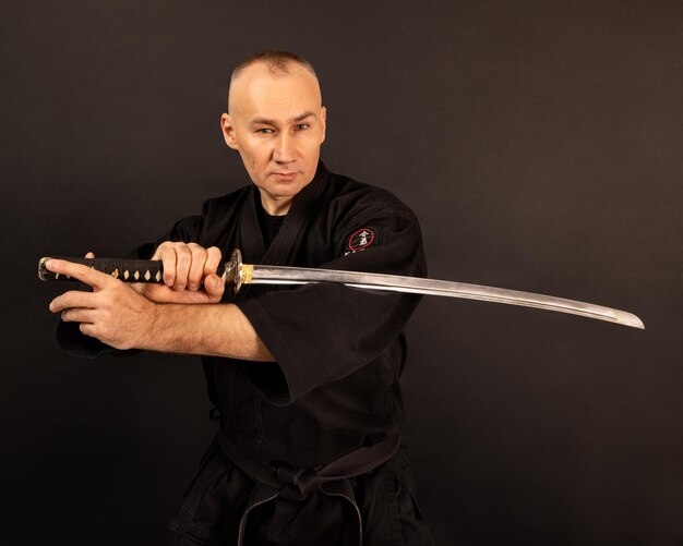 Foto retrato de um mestre de aikido com cinto de sensei preto em kimono de taekwondo com a espada katana