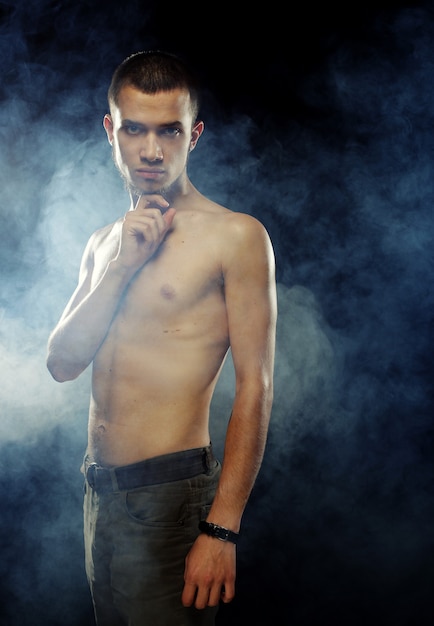 Retrato de um modelo masculino musculoso contra um fundo escuro com fumaça.