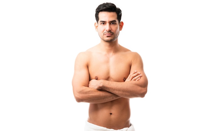 Retrato de um modelo masculino musculoso em pé sem camisa com os braços cruzados no fundo branco