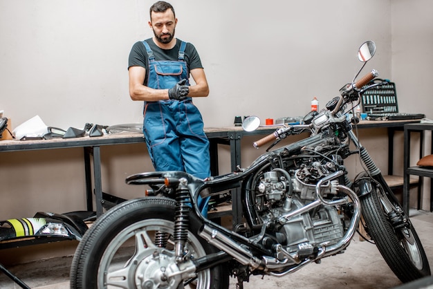 Retrato de um motociclista de macacão de trabalho em pé perto das motocicletas durante o conserto na oficina