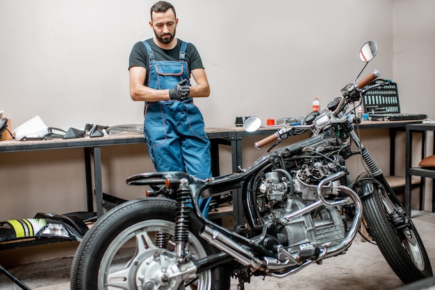 Foto retrato de um motociclista de macacão de trabalho em pé perto das motocicletas durante o conserto na oficina