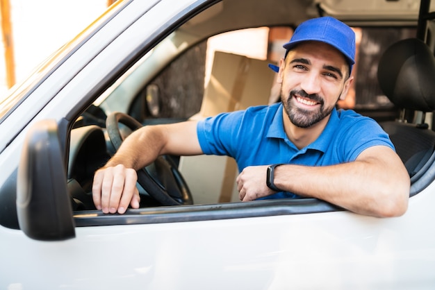 Retrato de um motorista de entregador dirigindo van com caixas de papelão no assento. Serviço de entrega e conceito de transporte.