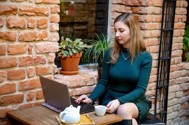 Retrato, de, um, mulher jovem, freelancer, usando computador laptop, para, trabalho à distância, enquanto, sentando, em, café moderno, com, xícara chá
