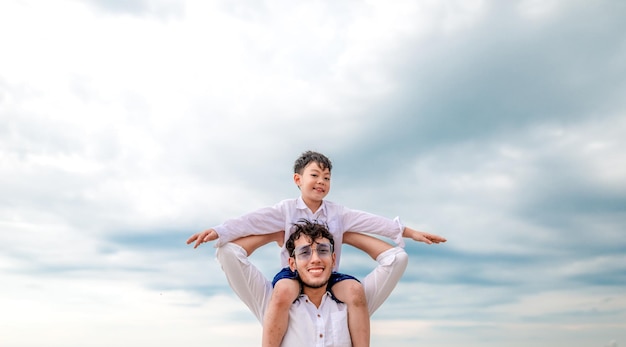Retrato de um pai carregando seu filho no ombro contra o céu