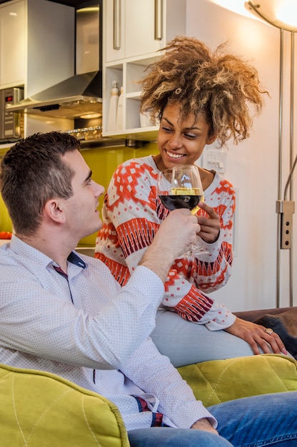 Retrato de um par de vidros de vinho no sofá em casa. Feliz casal sorridente que brilha seus copos de vinho. Eles estão sorrindo e bebendo suas bebidas