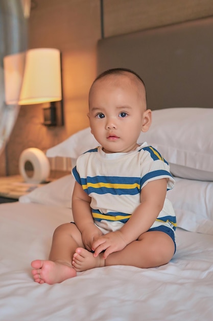 Retrato de um pequeno feliz menino asiático de 6 meses sentado na cama em casa