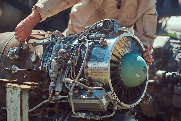 Retrato de um piloto-mecânico de uniforme e capacete voador, reparando a turbina desmontada do avião em um museu ao ar livre.