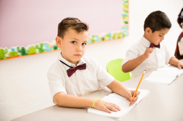 Retrato de um pré-escolar caucasiano bonito tomando algumas notas em seu caderno e fazendo contato visual