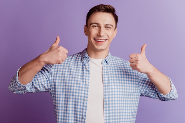 Retrato de um promotor alegre e confiável mostrando o polegar para cima para aprovar a solução em fundo violeta