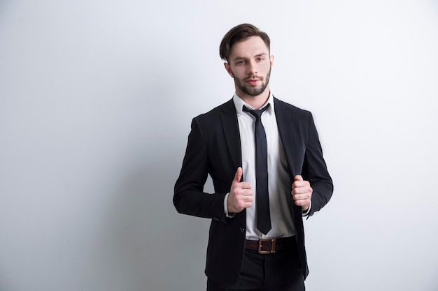 Retrato de um sério jovem empresário barbudo de pé perto de uma parede branca. Conceito de uma carreira em negócios. Mock up.