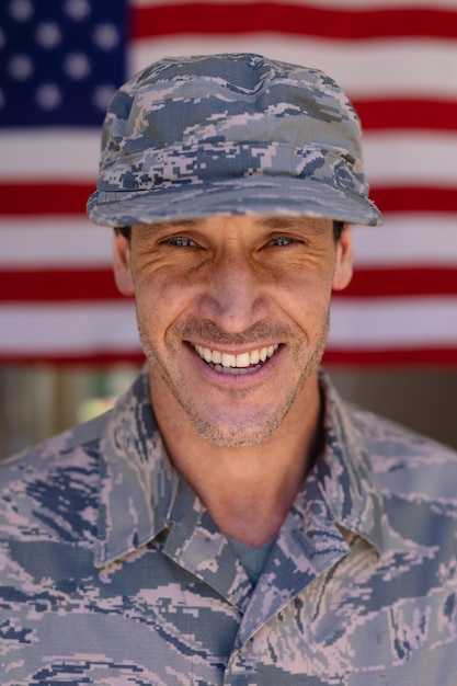 Retrato de um soldado do exército caucasiano sorridente usando boné e uniforme de camuflagem contra a bandeira dos EUA. conceito de pessoas, patriotismo e identidade, inalterado