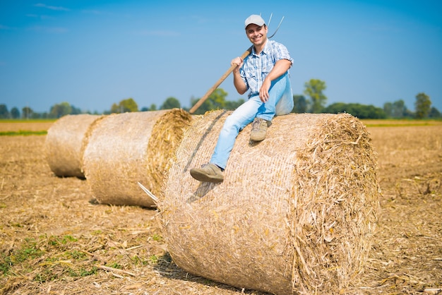 Retrato, de, um, sorrindo, agricultor, sentando, ligado, um, feno, pacote, em, seu, campo