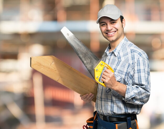 Foto retrato, de, um, sorrindo, carpinteiro, segurando, um, prancha madeira, e, um, serra, em, um, local construção