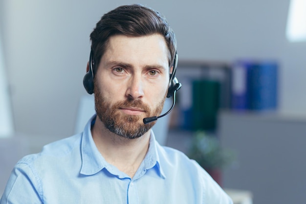 Retrato de um técnico masculino sério em uma loja, um homem olhando para a câmera pensativa usa um fone de ouvido para uma videochamada