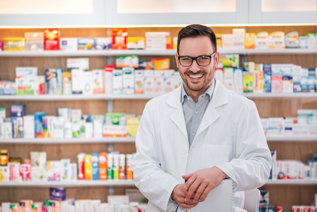 Retrato de um trabalhador alegre dos cuidados médicos no revestimento branco na loja farmacêutica.